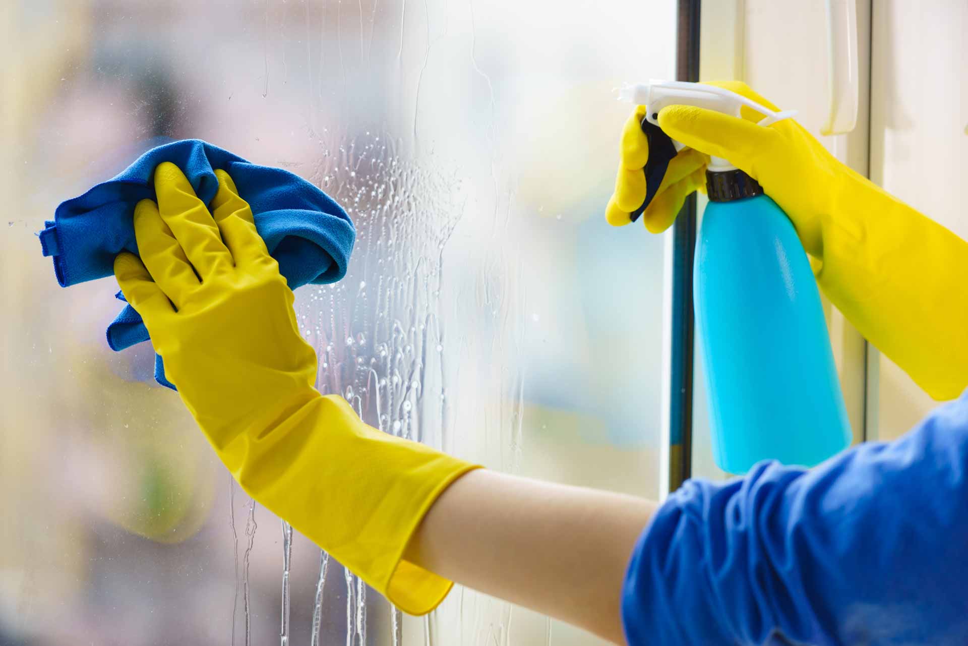 Person in yellow gloves cleaning a window